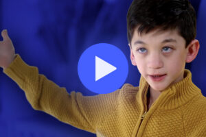 A young boy in a mustard yellow sweater gestures with his left arm extended. A blue play button icon is overlaid on the image, and the background is blurred in blue tones.
