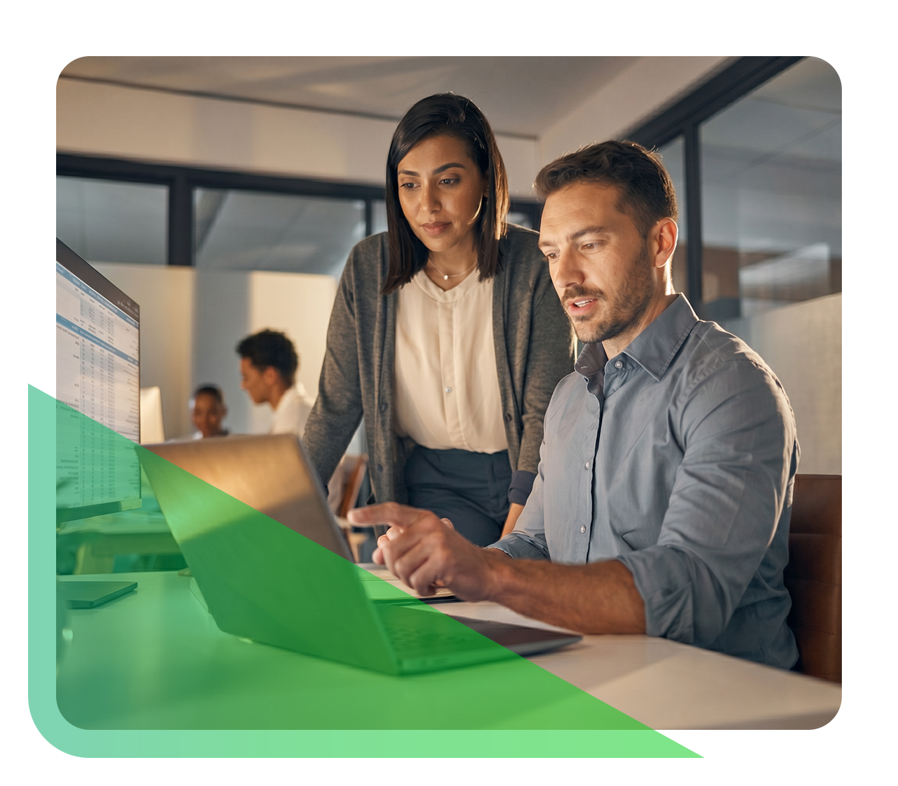 Two coworkers discuss payer contracting while looking at a laptop screen in a modern office, with other colleagues working in the background.