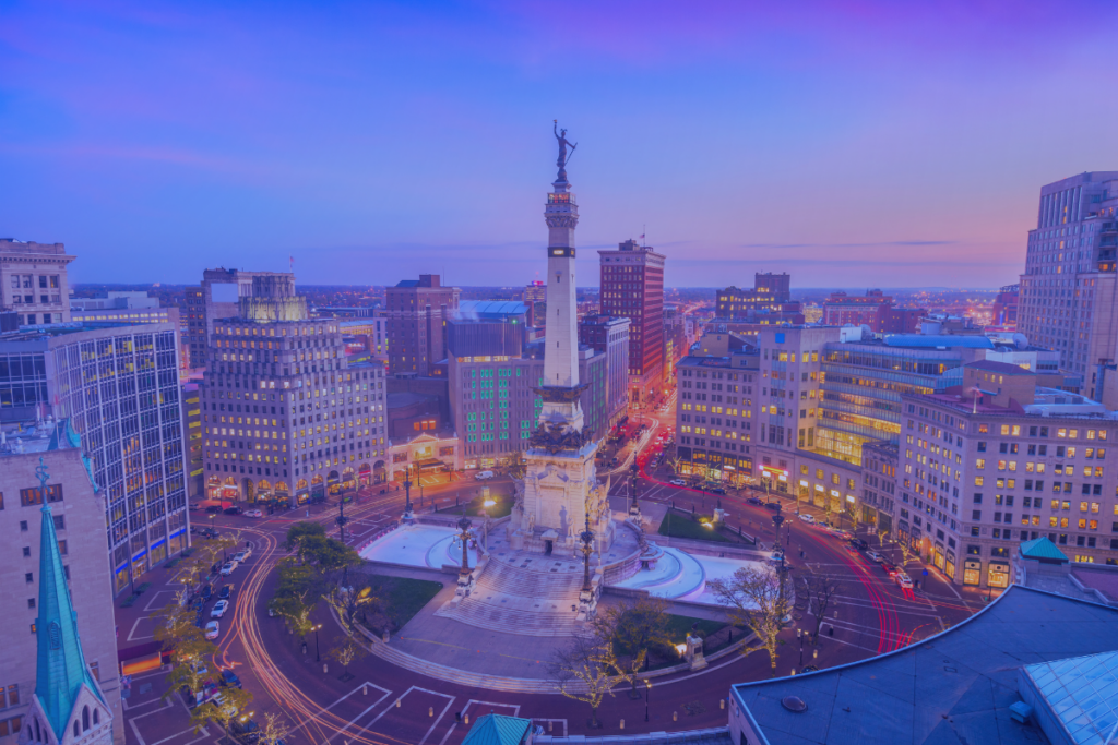 Aerial view of Monument Circle in downtown Indianapolis at dusk, with surrounding buildings and city lights visible under a purple sky, reminiscent of vibrant cityscapes like those near Stamford Health.