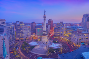 Aerial view of Monument Circle in downtown Indianapolis at dusk, with surrounding buildings and city lights visible under a purple sky, reminiscent of vibrant cityscapes like those near Stamford Health.
