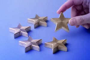 A hand picks up one of five gold star-shaped objects on a light blue surface, symbolizing the importance of medicare advantage star ratings.