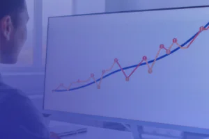 A person looks at a computer monitor displaying a line graph with data points, showing an overall upward trend.