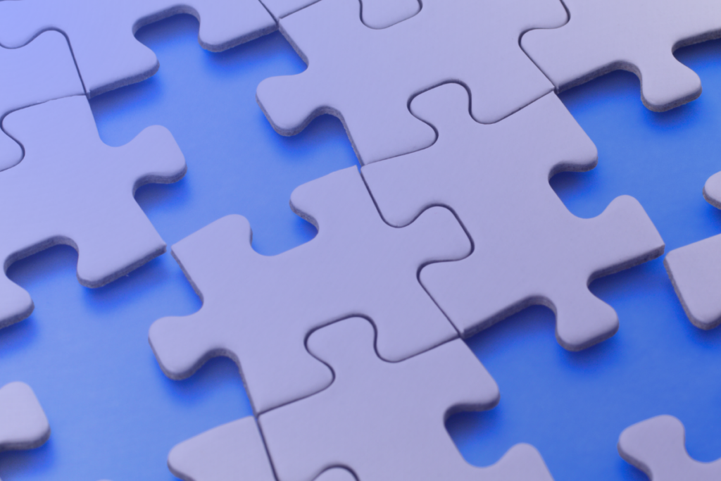 Several white puzzle pieces, representing denials management, lie on a blue surface—some connected and some separated—with soft lighting creating a slight purple tint.